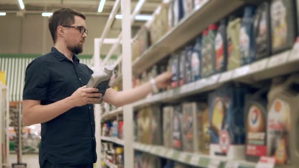 Mannelijke chauffeur neemt uit een verschillende flessen met olie voor de auto in een winkel — Stockvideo