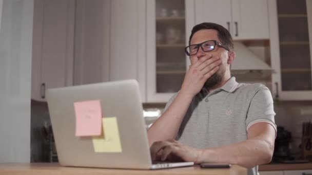 El hombre agotado está trabajando con cuaderno en la noche en la cocina y bostezando — Vídeos de Stock