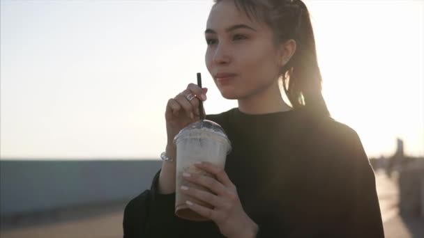 Joven morena está bebiendo café con leche helada a través de paja en muelle por la noche — Vídeos de Stock