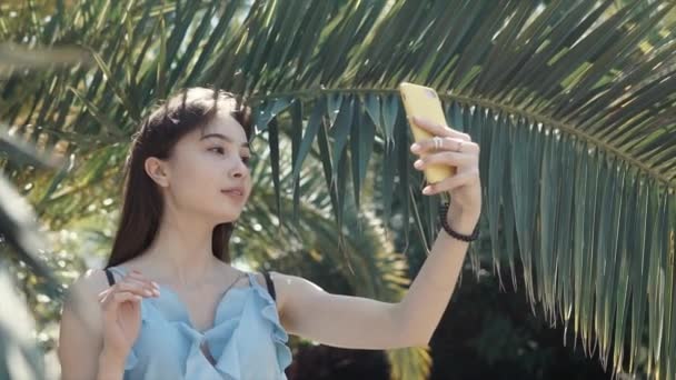 Маленькая стройная женщина делает селфи на камеру своего смартфона в летнем саду — стоковое видео