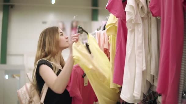 Chica está tomando camiseta de percha en una tienda y poner otros en rack — Vídeos de Stock