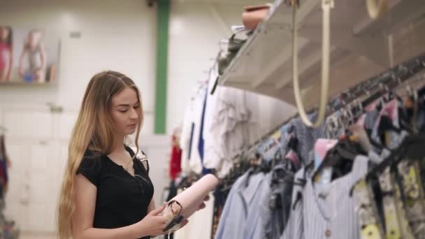 Fille blonde admire sac à main féminin à la mode dans un magasin, tournant dans les mains — Video