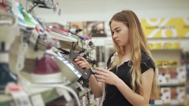 Blonde tient en main un échantillon d'exposition d'un fer à repasser dans un supermarché — Video
