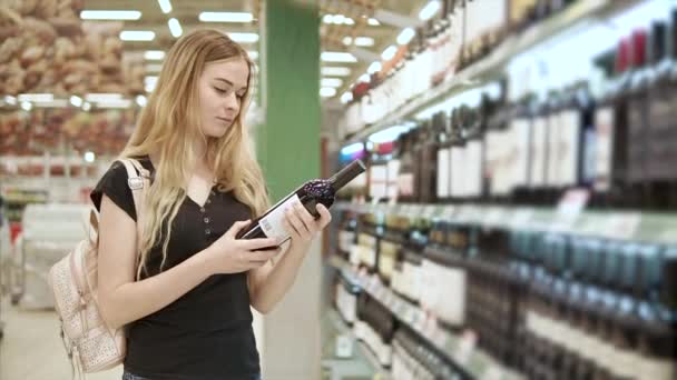 Mujer rubia adulta está leyendo inscripciones en una botella de vino en un supermercado — Vídeos de Stock