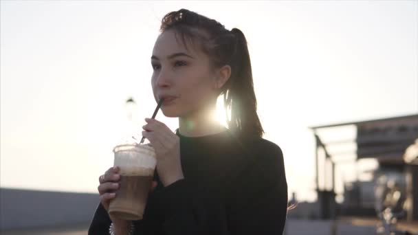 Vrolijke tienermeisje is nippen koude koffie op een straat in avond — Stockvideo