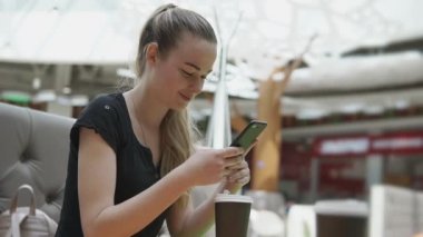 Neşeli kadın kahve ve cep telefonu ile bir alışveriş merkezinde bir kafede dinleniyor