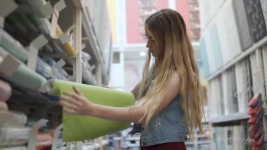 Genç tek kadın wallcovering bir rulo raf bir dükkanda alıyor