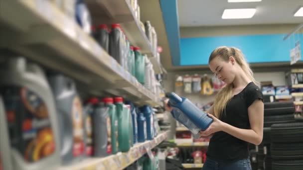 Jeune femme lit des étiquettes sur des bouteilles avec de l'huile de machine en magasin — Video