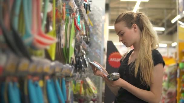 Joven anfitriona está examinando cucharones en un pasillo en un hipermercado — Vídeo de stock