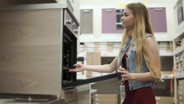 Szőke lány vizsgálja a modern tűzhely sütővel, az üzletben — Stock videók