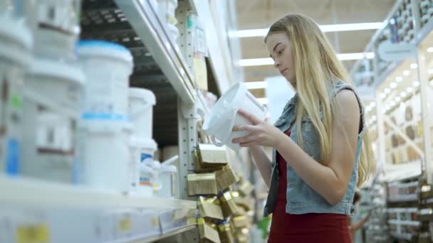 Diseñadora femenina está examinando ollas con pinturas en una tienda, tomando diferentes tipos — Vídeo de stock