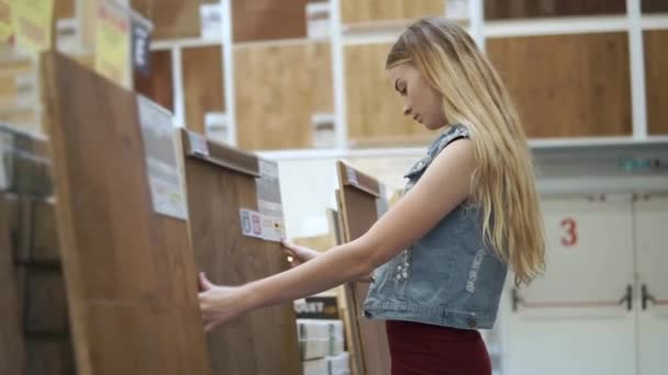 Blonde vrouw is het aanraken van een grote houten paneel voor vloerbedekking in een winkel — Stockvideo