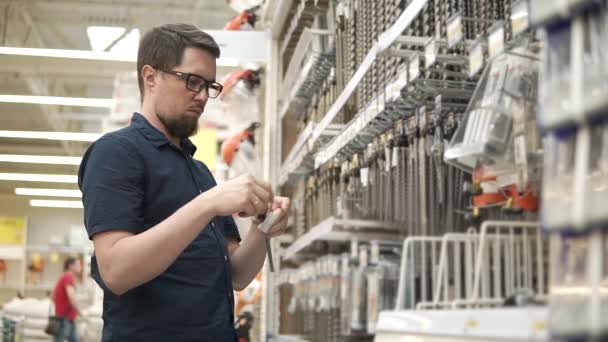 Male shopper is taking big metal drill bit from racks in a shop for builders — Stock Video