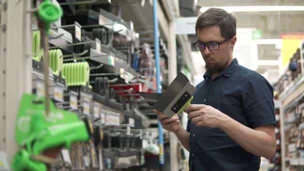 El hombre sostiene dos palas de metal en las manos en un departamento de la tienda para los constructores — Vídeos de Stock