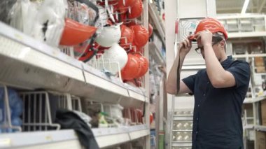 Sakallı adam inşaat kask hipermarket yapanlar için seçmektir. O bir hall salonu ve turuncu şapka çalışırken duruyor