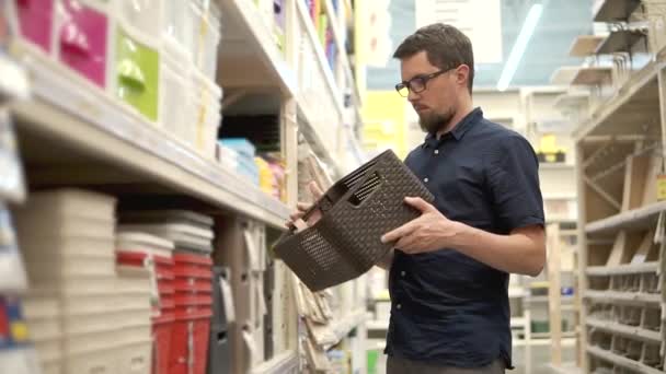 Man kijkt naar een kunststof mand in een supermarkt, twirling het in de hand — Stockvideo