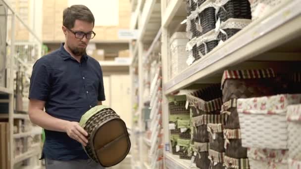 El hombre está tomando diferentes cestas tejidas de bastidores en una tienda, eligiendo — Vídeo de stock