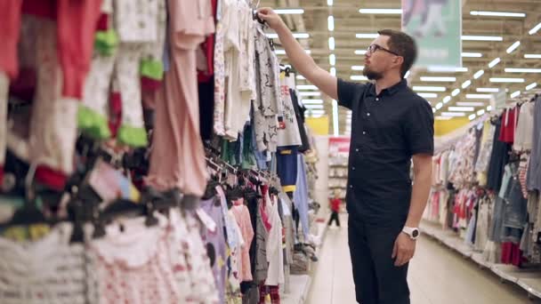 Joven padre está eligiendo ropa en un departamento de niños en la tienda — Vídeos de Stock