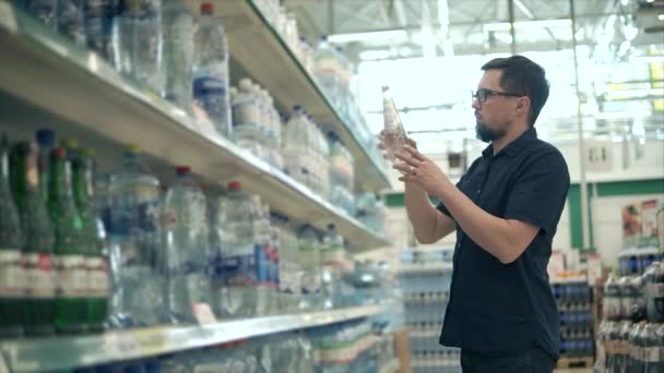 Клиент берёт с полки две бутылки с минеральной водой и читает — стоковое видео