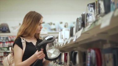 Genç güzel kadın mağaza raf yakınındaki elektrikli su ısıtıcısı örneği inceliyor