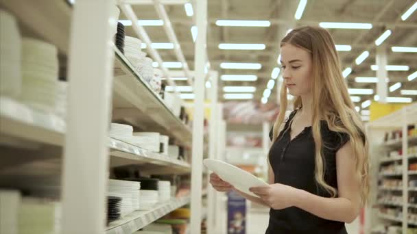 Femmina shopper sta guardando piatto di ceramica bianca in una sala del supermercato — Video Stock