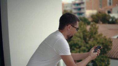 Alone yakışıklı adam, akıllı telefon kullanarak, balkonda yalnız duruyor