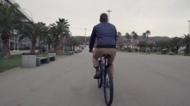 Adam tropikal şehirde yol üzerinden yaz gününde bisiklet sürme, arka görünüm