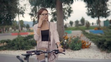 Genç townswoman Bisiklet tutarak, mobil açık havada konuşuyor