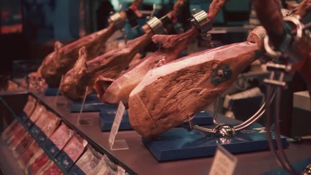 Jamons stojí na výkladní skříni na tradičním španělském trhu, na prodej — Stock video