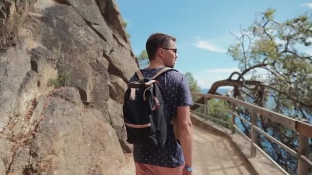 Дорослий чоловік ходить один на вузькому шляху на схилі пагорба в сонячний день, вид ззаду — стокове відео