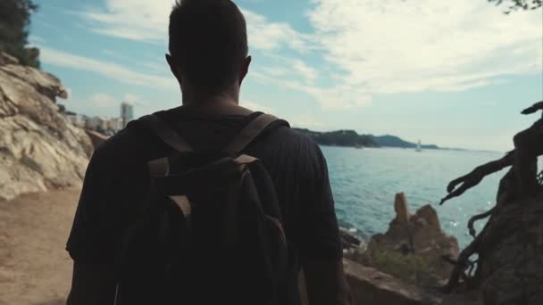 Человек турист выходит из темной пещеры на солнечной области с морской и городской пейзаж — стоковое видео