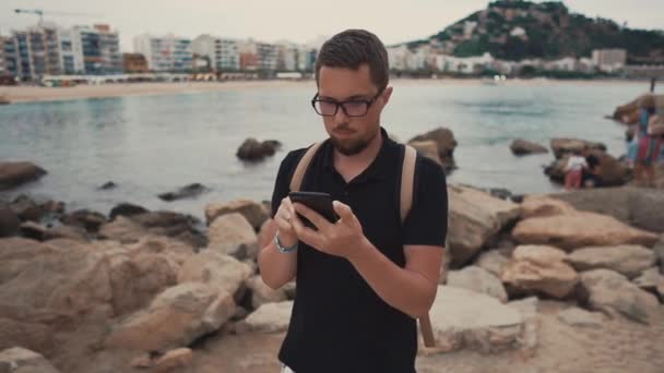 Un homme regardant son téléphone sur un rivage . — Video