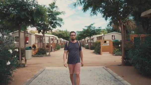 Barbudo turista está caminando en el patio de la zona turística con pequeñas cabañas de verano — Vídeo de stock