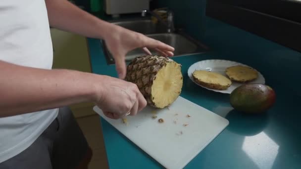 A felnőtt férfi egzotikus gyümölcsöket szeletel a konyhaasztalon, közelről — Stock videók