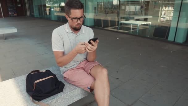 Чоловік відпочиває на лавці в місті, використовуючи смартфон з Wi-Fi — стокове відео
