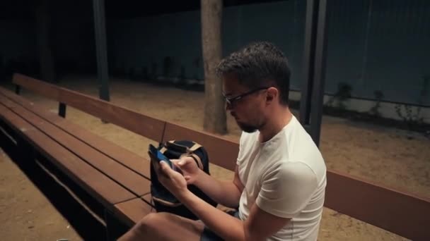 Один чоловік сидить в парку ввечері, шукаючи мережу для телефону — стокове відео