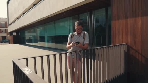 Adult bearded man is typing sms on screen of smartphone standing outdoors — Stock Video