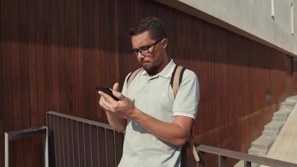 Solo hombre de pelo oscuro está tocando en la pantalla táctil del teléfono móvil al aire libre — Vídeos de Stock