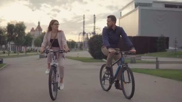 Двое друзей мужчина и женщина едут на велосипедах в город вечером, разговаривают друг с другом — стоковое видео