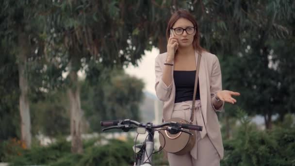 Young indignant woman is talking by mobile phone in park in summer day — Stock Video