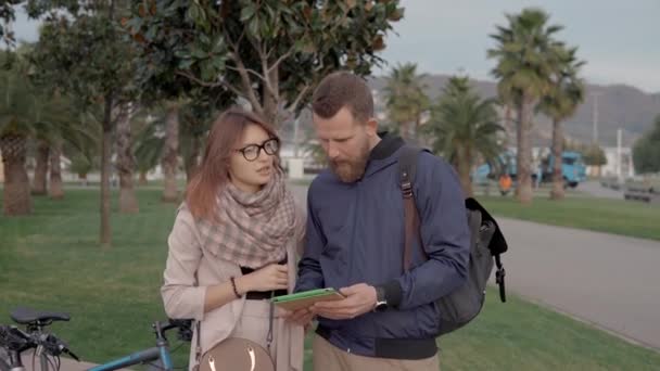 Пара велосипедистов обсуждают карту парка, стоящего на открытом воздухе в летний вечер — стоковое видео