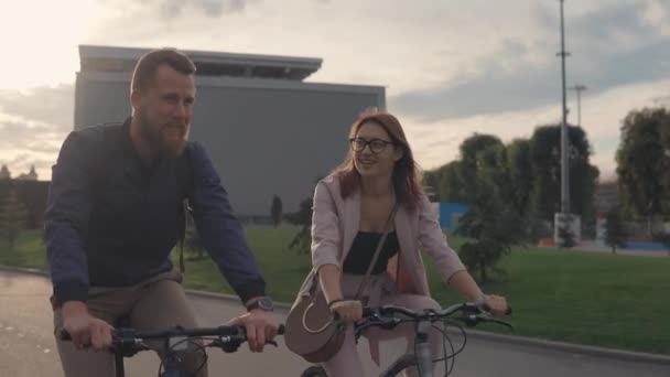 Jovem e sua namorada estão andando de bicicleta em uma cidade na noite de verão — Vídeo de Stock