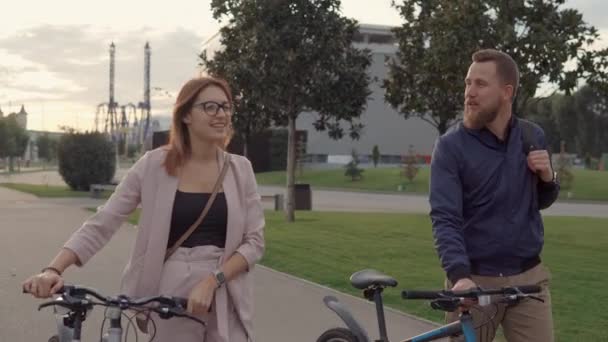 Gli amanti felici stanno camminando insieme nel parco, rotolando le loro biciclette vicino — Video Stock