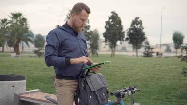 Homem usando tablet ao ar livre em uma bicicleta . — Vídeo de Stock