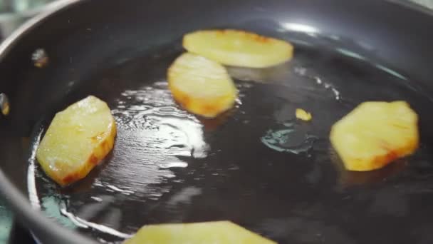 Повар трясет кастрюлю с кусочками ананаса в масле, стоящим на плитке, крупным планом — стоковое видео