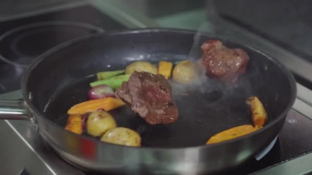 Man is frying two pieces of beef and vegetables in pan, close-up view — Stock Video