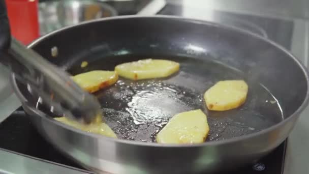 ジューシーなパイナップルの作品は、キッチンで鍋に揚げている、クックはそれらを移動している — ストック動画