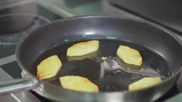 Pieces of pineapple are frying in boiled olive oil in pan, cook is shaking, — Stock Video