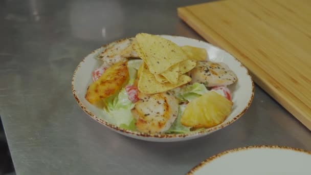 Piatto con deliziosa insalata Cesar è sul tavolo, cuoco sta aggiungendo patatine in cima — Video Stock