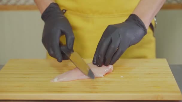 Кухар нарізає сире куряче філе на дерев'яній дошці, крупним планом — стокове відео